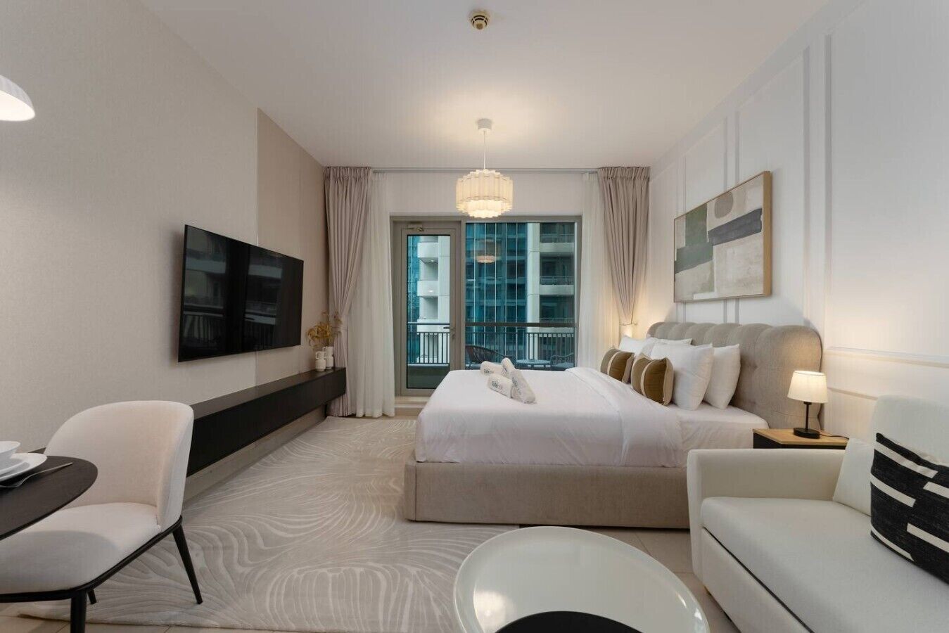 Quarto de hotel com cama, escrivaninha, cadeira, televisão e janela com vista para edifícios.