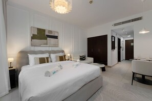 Ein Hotelzimmer mit einem großen Bett, Nachttischen, einer Couch, einem Esstisch mit Stühlen und einem Flur, der zu einem Kleiderschrank führt.