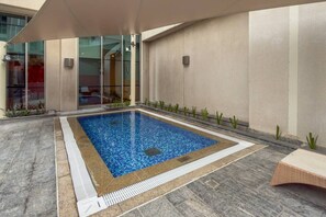 Ein rechteckiger Pool im Freien mit einer gefliesten Kante, umgeben von einer niedrigen Steinmauer und einem überdachten Bereich mit einem Sonnensegel.