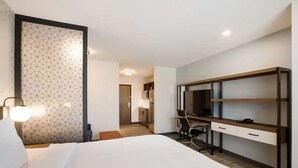 A hotel room with a bed, a desk with a chair, a TV, and a kitchenette in the background. - Near The Shops at Dos Lagos | Full Kitchen & Gym (Corona)