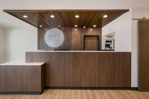 A reception desk with a wooden finish, a circular logo, and a door to the right. - Near The Shops at Dos Lagos | Full Kitchen & Gym (Corona)