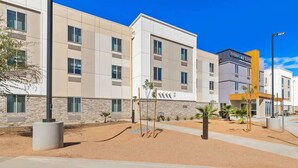 A modern hotel building with multiple floors, a sign for 'EVERHOMESUITES', and a landscaped area with palm trees. - Near The Shops at Dos Lagos | Full Kitchen & Gym (Corona)