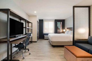A hotel room with a bed, a desk with a computer, a television, a sofa, and a window. - Near The Shops at Dos Lagos | Full Kitchen & Gym (Corona)