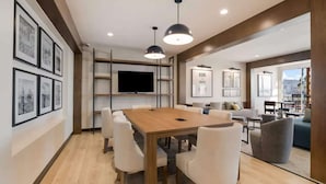 A modern conference room with a wooden table, white chairs, a flat-screen TV, and framed pictures on the walls. - Near The Shops at Dos Lagos | Full Kitchen & Gym (Corona)