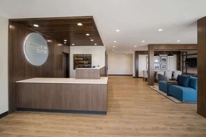 A hotel reception area with a wooden reception desk, a circular sign, and a seating area with a blue sofa. - Close to The Shops at Dos Lagos | Full Kitchen (Corona)