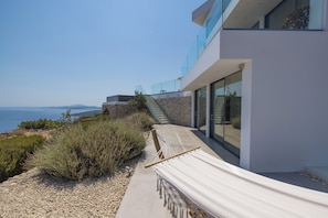 A modern building with a stone wall, a hammock, and a view of the sea. - The Luminous Villa: private estate, 4 sea-view suites, heated pool, sleeps 8 (Volimes)