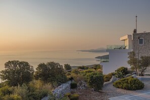 Un bâtiment moderne avec une façade en pierre, un balcon doté d’une balustrade en verre et une vue sur la mer.