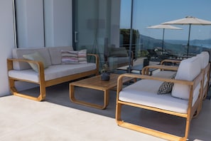 A modern outdoor seating area with a sofa and chairs, a wooden coffee table, and a glass table with a view. - The Luminous Villa: private estate, 4 sea-view suites, heated pool, sleeps 8 (Volimes)