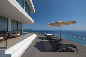 A modern outdoor deck with lounge chairs and an umbrella, overlooking a pool and the ocean. - The Luminous Villa: private estate, 4 sea-view suites, heated pool, sleeps 8 (luminous villa)