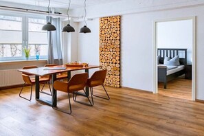 Een eetgedeelte met een houten tafel en stoelen, een wandmontage met houtblokken, en een bed in de aangrenzende kamer.