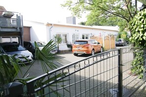 A residential area with a white building, a parked orange car, and a metal fence. - Holiday apartment with 1 bedroom (Warnemünde)