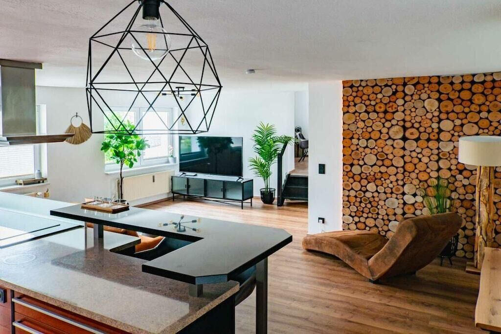 Een moderne woonkamer met een geometrische hanglamp, een flatscreen televisie en een wand versierd met houtblokken.