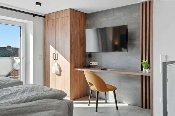 Quarto moderno com cama, escrivaninha, cadeira e televisão.