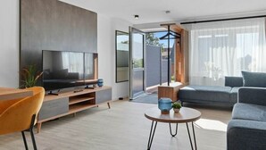 Uma sala de estar moderna com uma TV de tela plana, um sofá, uma mesa de centro e um espaço de jantar com uma cadeira.