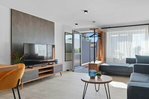 Una sala de estar moderna con una televisión de pantalla plana, un sofá, una mesa de centro y un comedor con una silla.