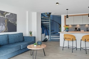 Uma sala de estar moderna com um sofá, uma mesa de centro redonda e uma escada que dá para uma área de cozinha.