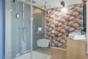 Un baño moderno con ducha envuelta en vidrio, inodoro y lavamanos con encimera de madera.