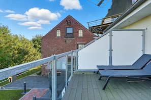 Une terrasse sur le toit, dotée d’une balustrade en verre, d’un fauteuil de relaxation et offrant une vue sur un immeuble en briques rouges.