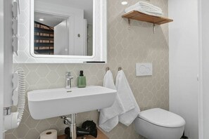 Un baño con lavamanos blanco, espejo, inodoro y toallero.