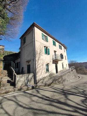 A two-story building with a balcony, a staircase leading to the entrance, and a paved road in front. - Castello della Regina: Panoramic Views, a Home Full of Relaxation and Comfort (Emilia-Romagna)