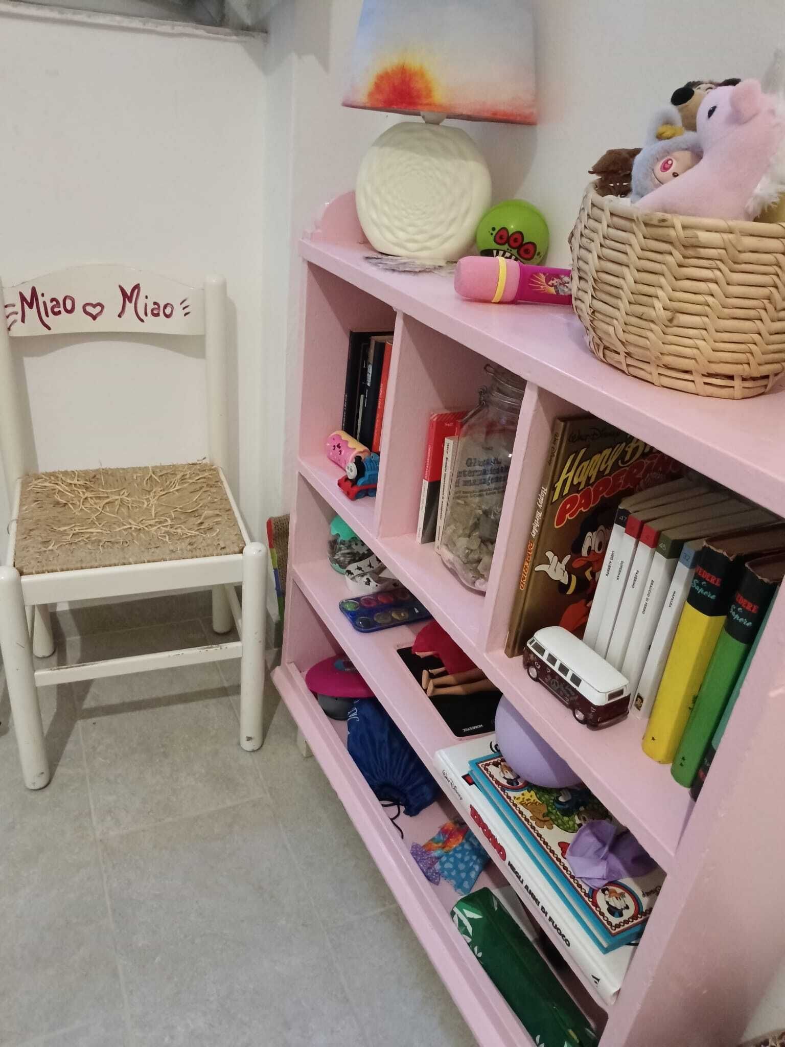 Una stanza con una sedia bianca, uno scaffale rosa e un cesto in cima.
