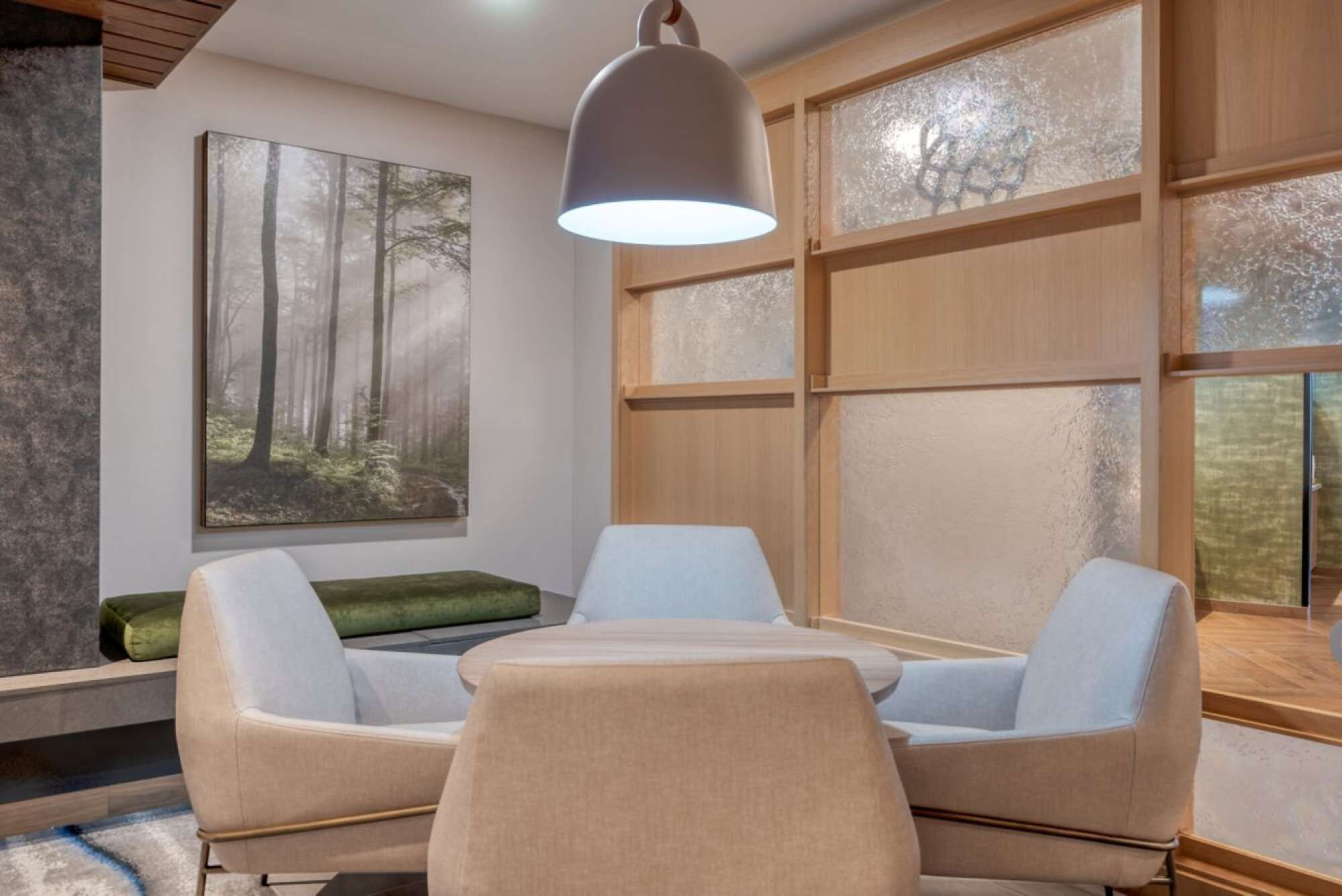 A modern room with a large window, a painting of a forest, a table with two chairs, and a hanging light fixture.