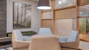 Une chambre moderne avec une grande fenêtre, un tableau représentant une forêt, une table avec deux chaises et un luminaire suspendu.