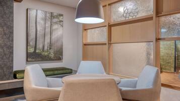 A modern room with a large window, a painting of a forest, a table with two chairs, and a hanging light fixture.