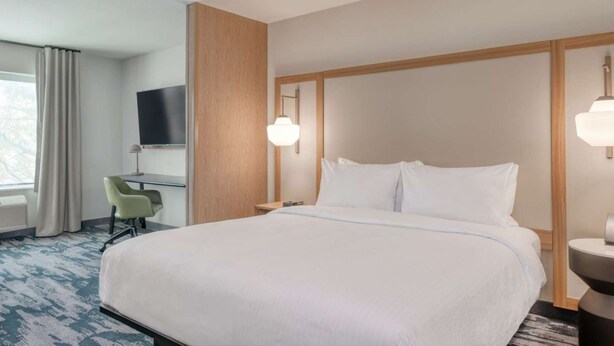 Ein Hotelzimmer mit einem großen Bett, einem Schreibtisch mit Stuhl, einem Fernseher und einem Fenster mit Vorhängen.
