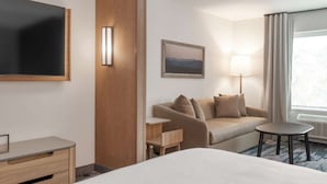Ein Hotelzimmer mit Bett, Schreibtisch, Sofa, Lampe, einem Bild und einem Fenster mit Vorhängen.