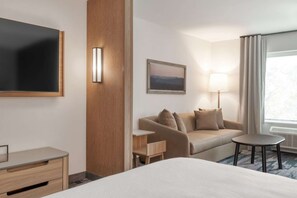 A hotel room with a bed, a desk, a sofa, a lamp, a painting, and a window with curtains. - Close to The Outlet Shoppes + Free Breakfast & Gym (Shelbyville)