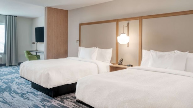 Ein Hotelzimmer mit zwei Betten, einem Schreibtisch, einem Sessel, einem Fernseher und einer Lampe.