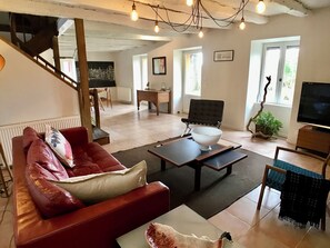 A living room with a red leather sofa, a white bowl on a coffee table, a black chair, a television, and a staircase.