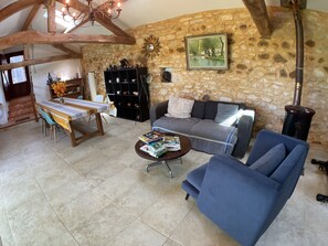 A cozy living room with a stone wall, a sofa, a coffee table with magazines, and a dining area with a table and chairs.