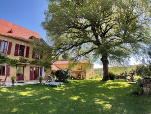 Una casa tradicional amb teulada vermella, un arbre gran al pati i un jardí ben cuidat.