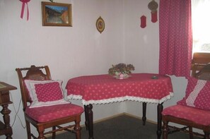A room with two wooden chairs, a table with a red tablecloth, and a small table with a vase of flowers. - Holiday home with 2 bedrooms (Nordstrand)