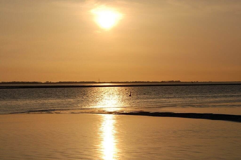 Un coucher de soleil sur une étendue d'eau calme, avec une plage au premier plan.