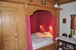 A wooden bed with a red canopy, a bedside table with a lamp, and a mirror on the wall. - Holiday home with 2 bedrooms (Nordstrand)