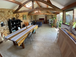 Une pièce spacieuse avec une longue table, des murs en pierre, des poutres en bois et une cheminée.