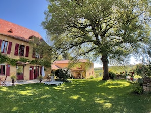 Een traditioneel huis met een rode dakbedekking, een grote boom in de voortuin en een verzorgd gazon.