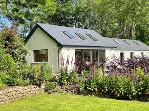 A house with a sloped roof, multiple windows, and a stone wall in the foreground. - A spacious one bed farm cottage, perfect for a relaxing getaway (Clonakilty)