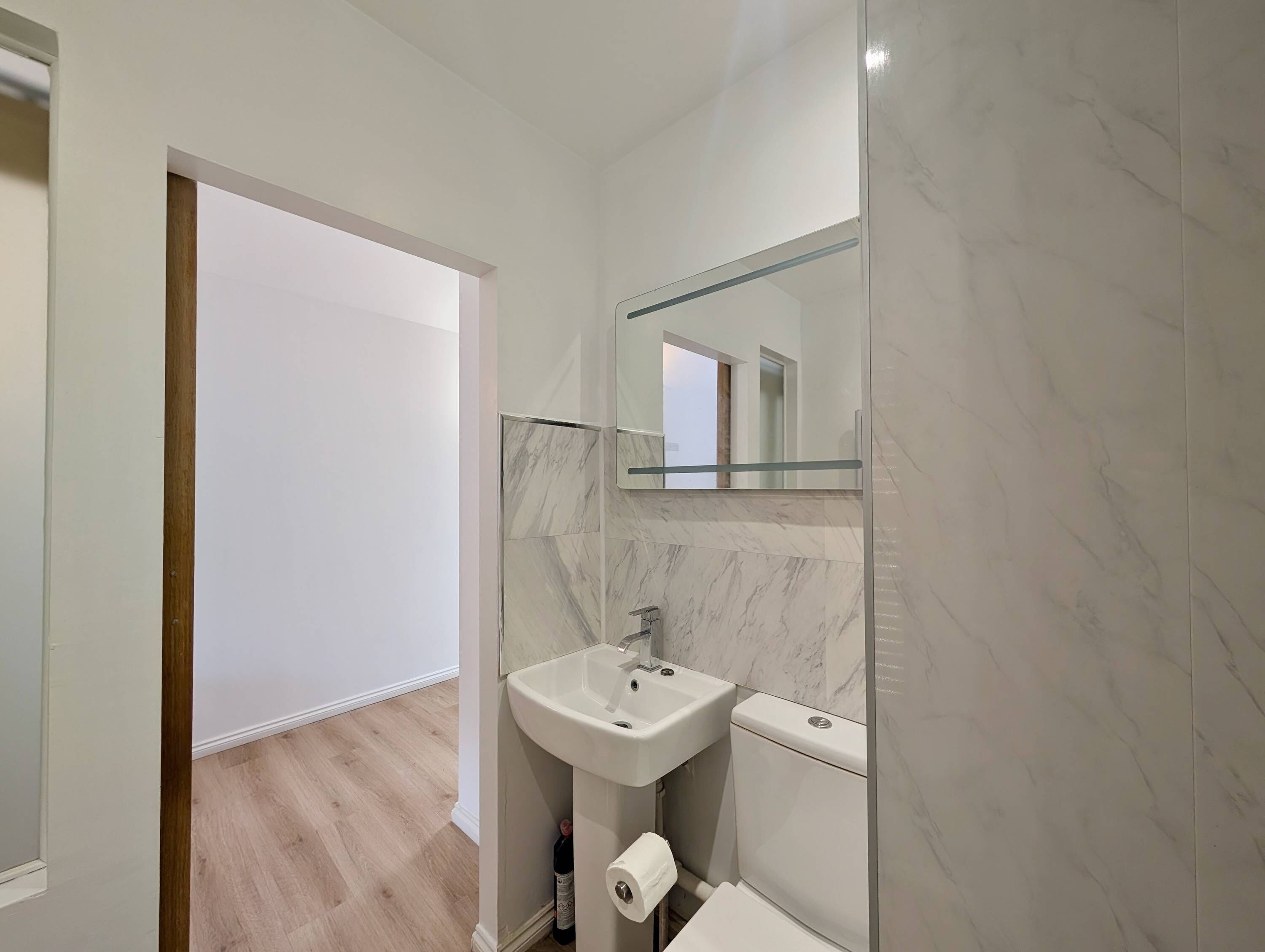 A modern bathroom with a marble wall, a sink, a toilet, and a mirror.