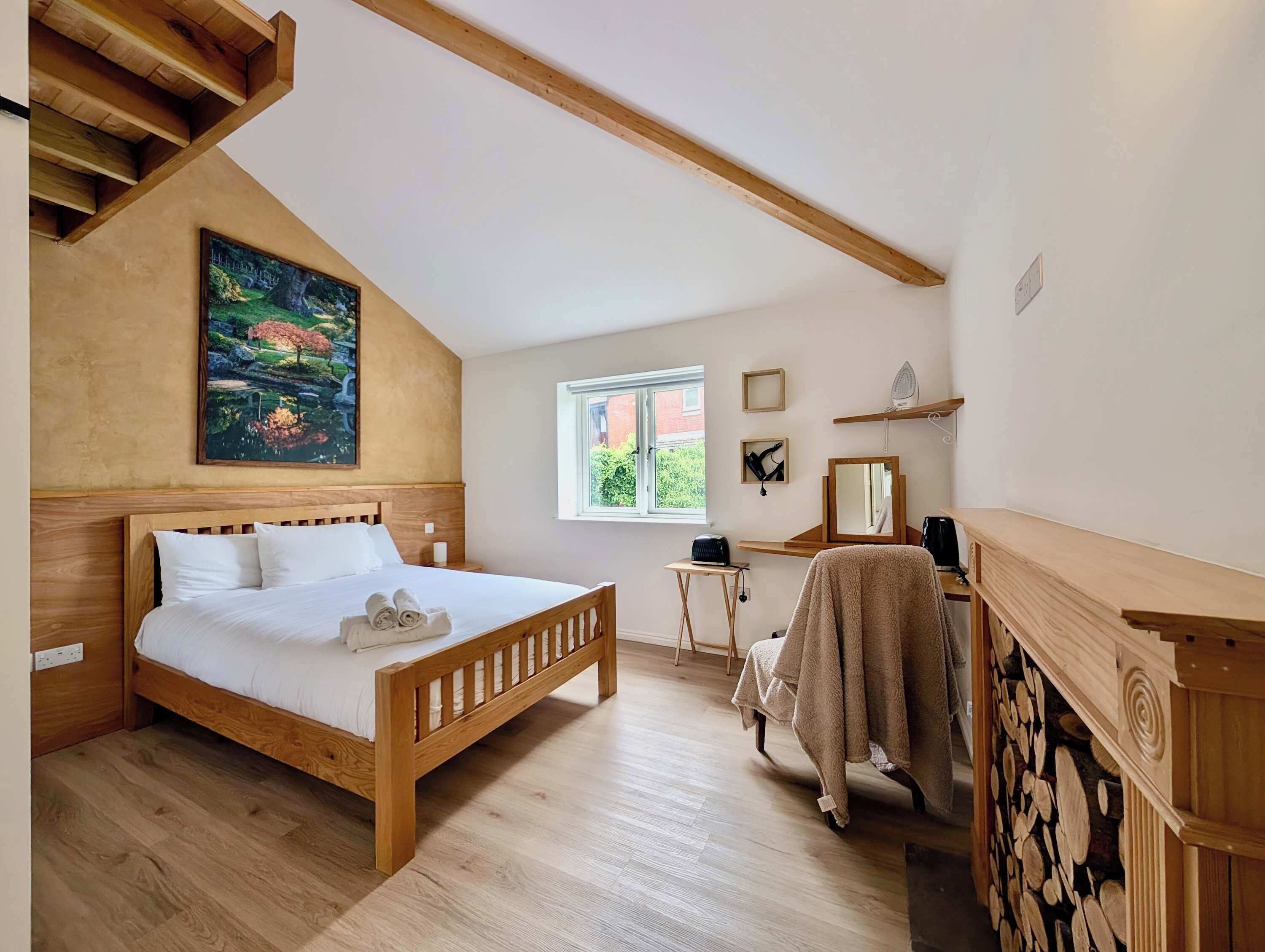 A bedroom with a wooden bed, a painting, a window, a desk, and a mirror.