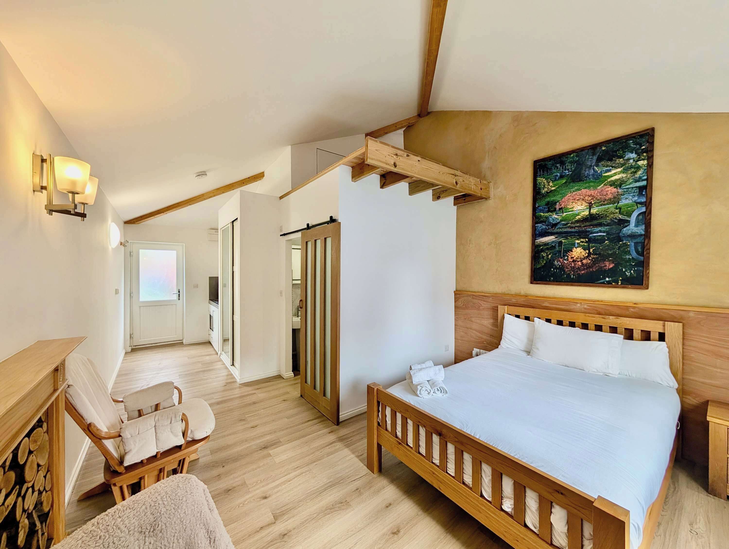 Une chambre à coucher avec un lit en bois, une chaise, un bureau et un tableau accroché au mur.