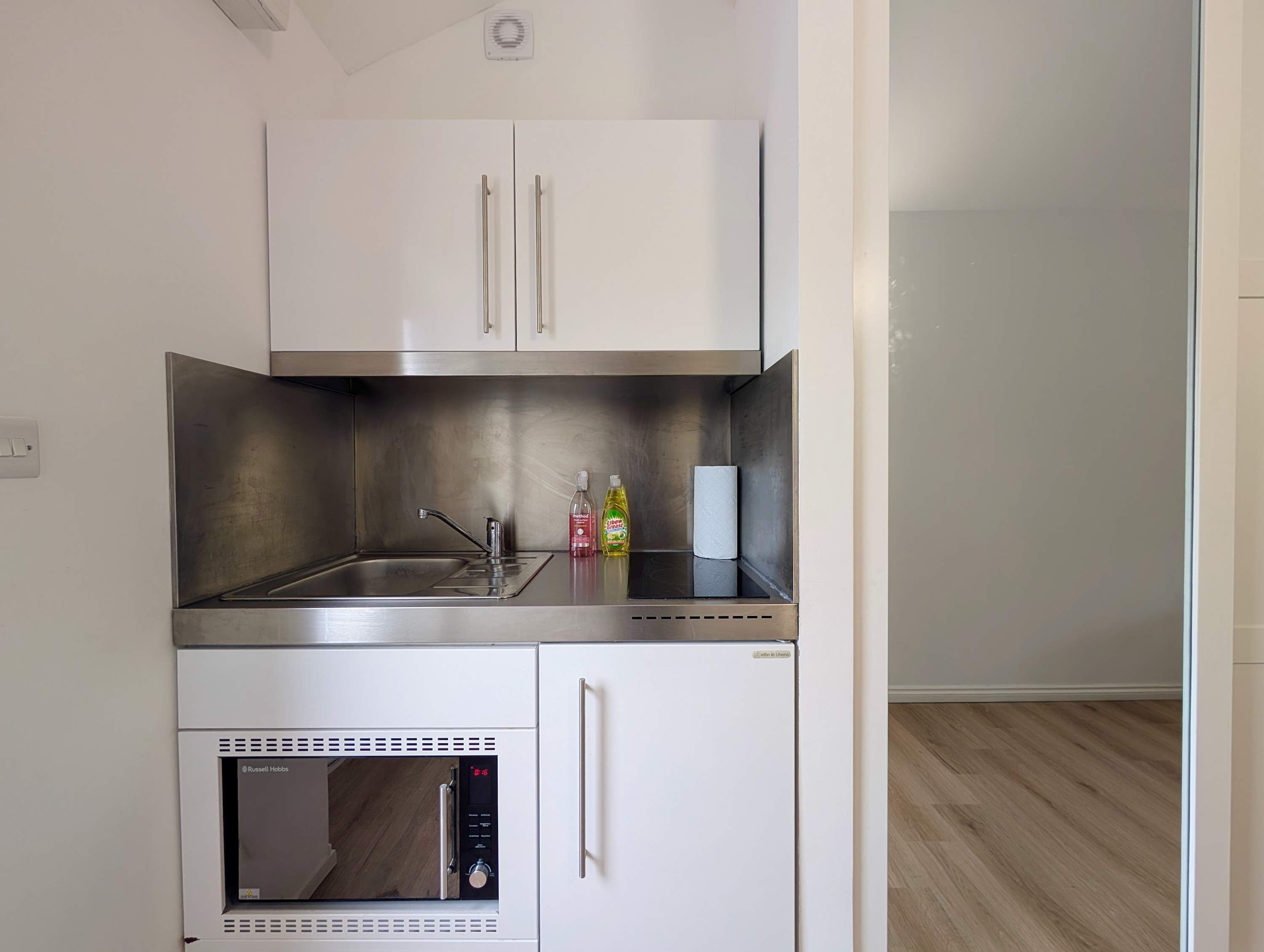 A compact kitchen with a built-in oven, a stainless steel sink, and a microwave.
