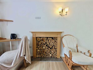 Una habitación acogedora con chimenea, un sillón, una mesa con hervidor y una lámpara de pared.