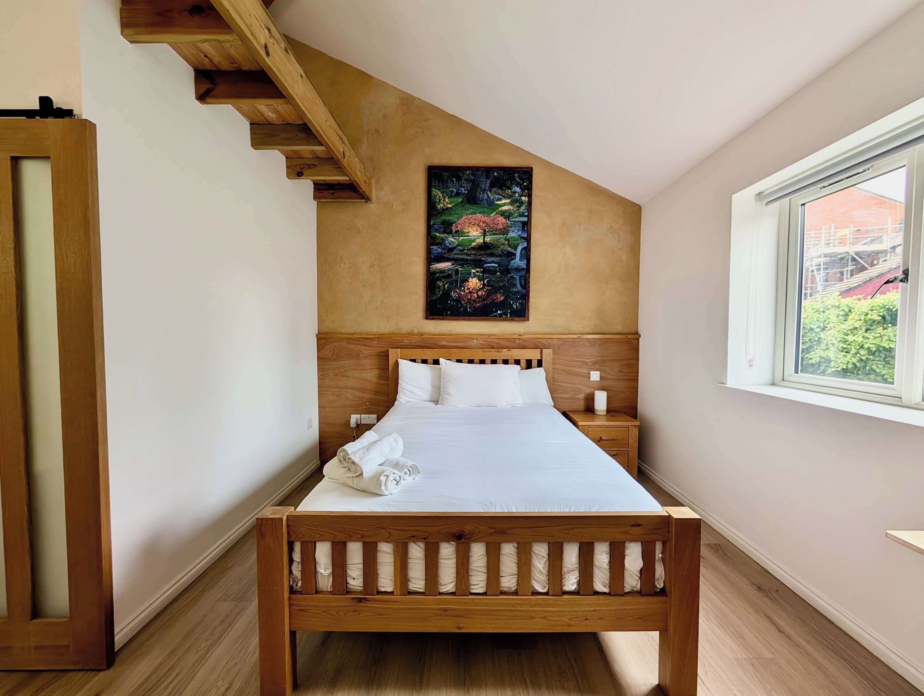 Quarto com cama de madeira, pintura na parede, janela com vista e escada de madeira.