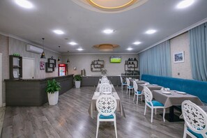 Un restaurante con una barra larga, sillas blancas y un banco acolchado azul.