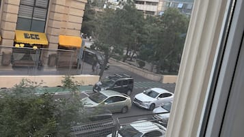 A view of a city street from a window, with tall buildings, parked cars, and a few pedestrians.