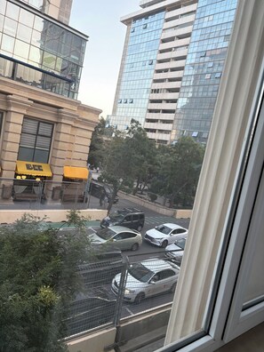 Vista de una calle urbana desde una ventana, con edificios altos, coches estacionados y algunas personas caminando.